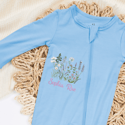 Light blue baby onesie with floral design and text on a woven mat