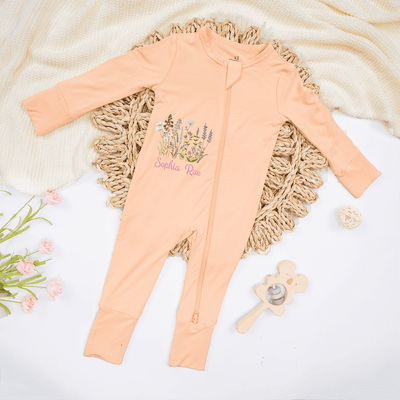 Peach-colored baby onesie with floral design and text on a textured surface with toys.