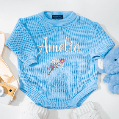 Blue baby romper with 'Amelia' and floral design, surrounded by toys on a white background