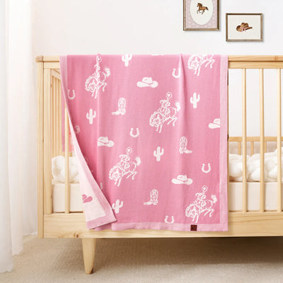 Pink blanket with white patterns draped over a crib in a nursery.