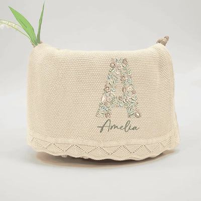 Beige personalized baby blanket with initals floral design and 'Amelia' text on a light gray background