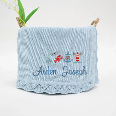 Blue personalized baby blanket with embroidered nautical designs and name 'Aiden Joseph' on a white background.