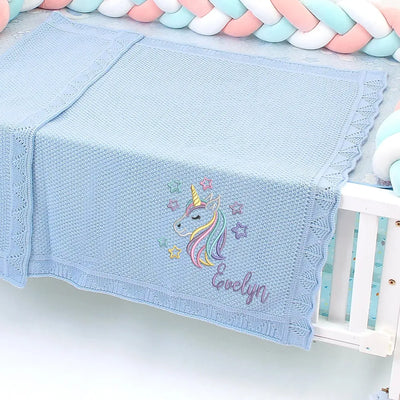 Light blue personalized baby girl blanket with unicorn design and embroidered name on a crib.