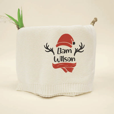 Cream personalzied baby blanket with a red Santa hat and black text on a beige background