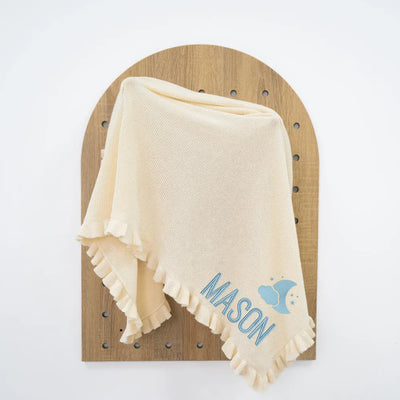 Cream personalized baby blanket with 'MASON' embroidery on a wooden board against a white background