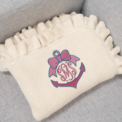 Cream personalized baby blanket with pink and blue anchor monogram design on a gray surface