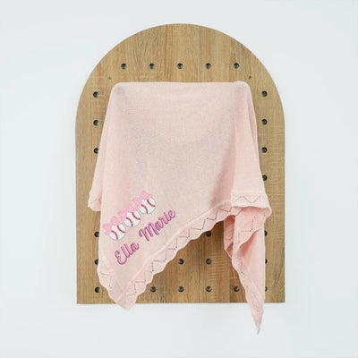Pink personalized baby blanket with embroidered names on a wooden board against a white background