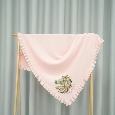 Pink personalized baby blanket with floral horse design on a wooden stand against a gray curtain background
